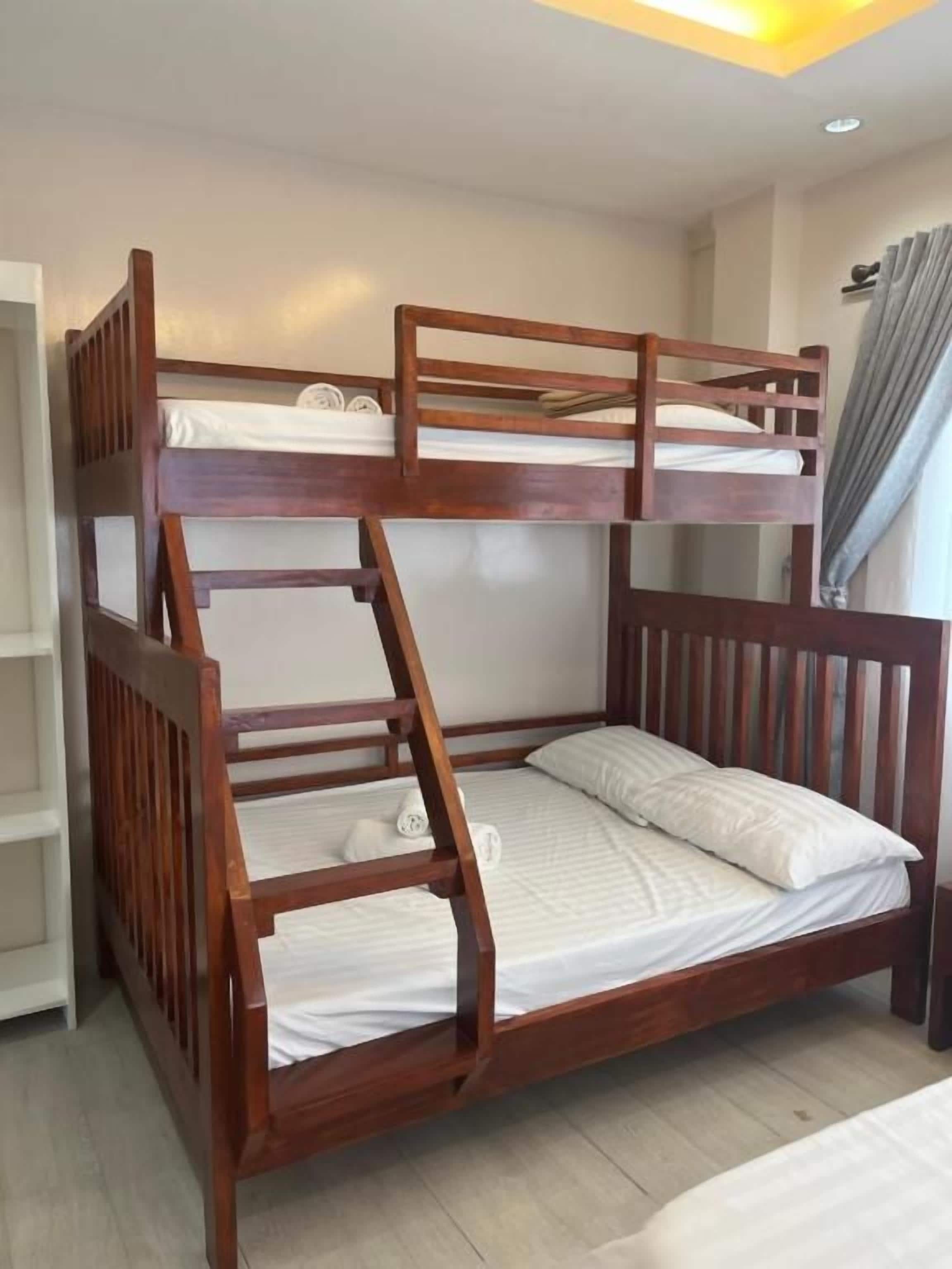 Een stapelbed met houten frame, wit beddengoed en een ladder.