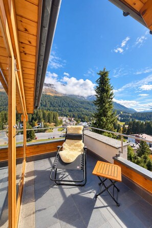 A balcony with a sun lounger, a small table, and a view of a mountainous landscape. - 1511 Foppa 26 by Interhome (Valbella)