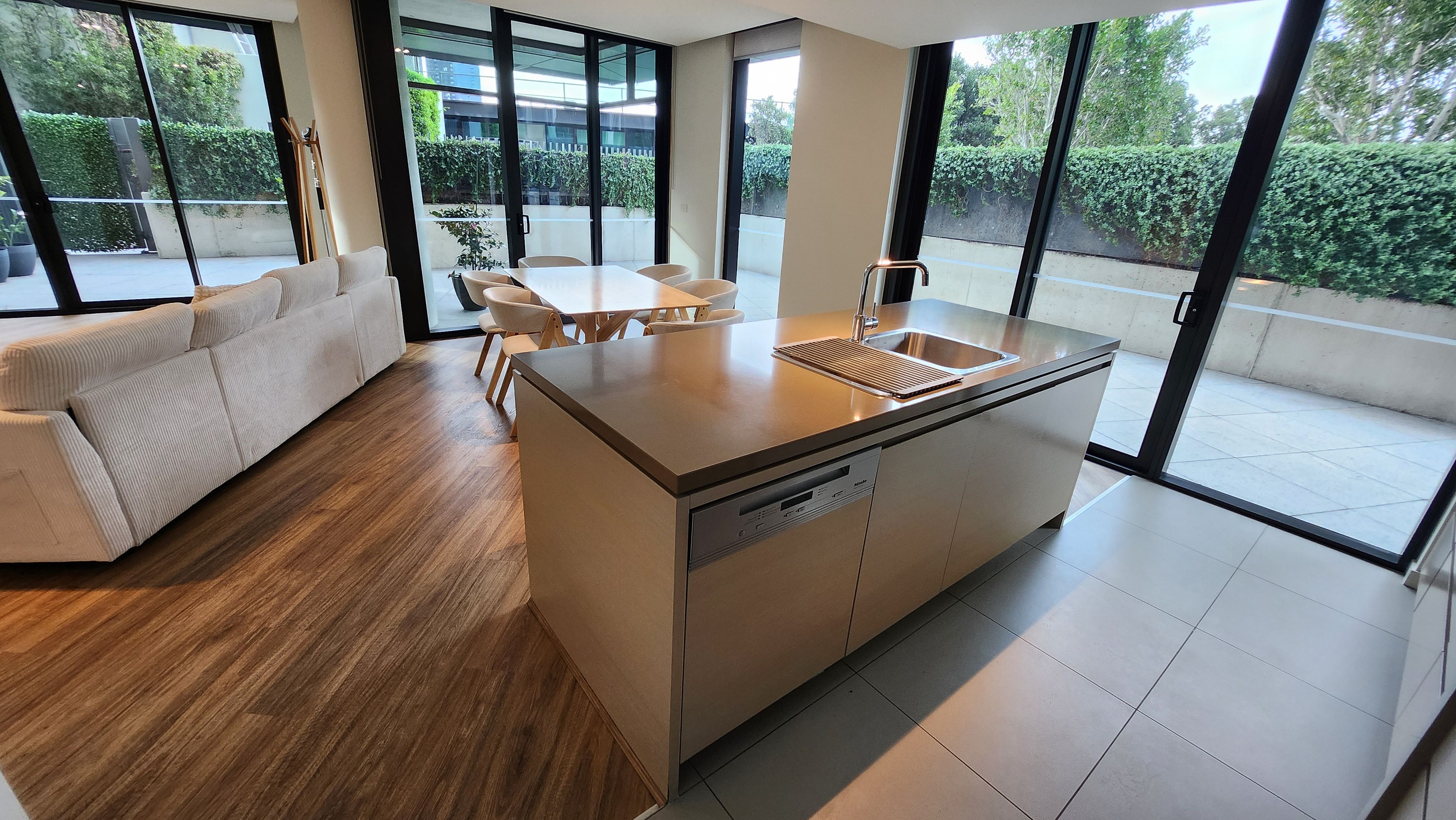 A modern kitchen with a built-in dishwasher, a dining area with a table and chairs, and large windows offering a view of the outdoors.