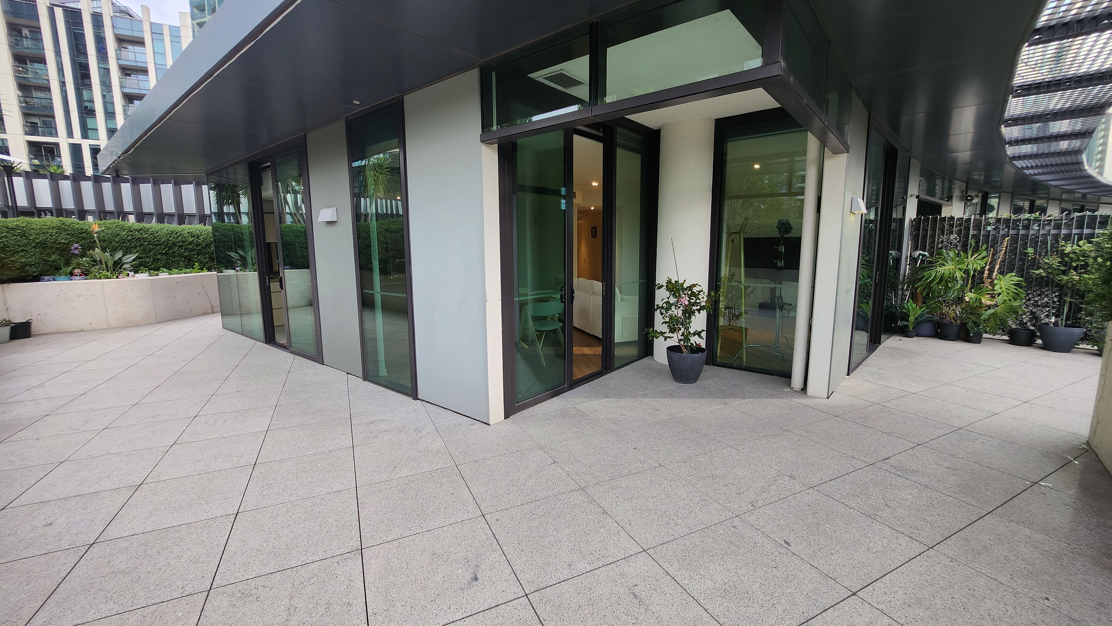 A modern building with large glass doors, a covered entrance, and a tiled patio area with potted plants.
