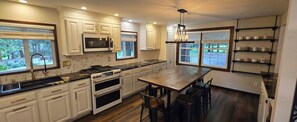 Une cuisine moderne avec des meubles blancs, un îlot central doté de tabourets de bar, un four à micro-ondes encastré et une cuisinière à gaz.
