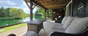 Un espace extérieur aménagé, abrité et doté de sièges, avec vue sur un lac, une table en osier et un canapé avec des coussins.