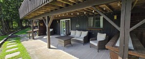 An outdoor patio area with a covered seating arrangement, a table, and a wooden deck. - Wilder Retreat Lodge near Letchworth - Private Pond, 5BR, Sleeps 10 (Warsaw)
