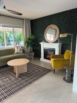 Ein Wohnzimmer mit Kamin, einer Couch, einem gelben Sessel und einem runden Couchtisch.