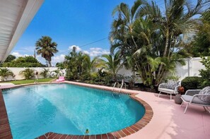 A swimming pool with a brick edge, surrounded by palm trees and a white fence. - Chic 2-Bedroom Home with Heated Pool + Bar close to AMI/IMG (Bradenton)