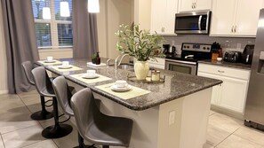 A modern kitchen with a central island, bar stools, a microwave, a stove, and a refrigerator. - The Magic House, Near Disney, Game Room, 10 Guests (Kissimmee)