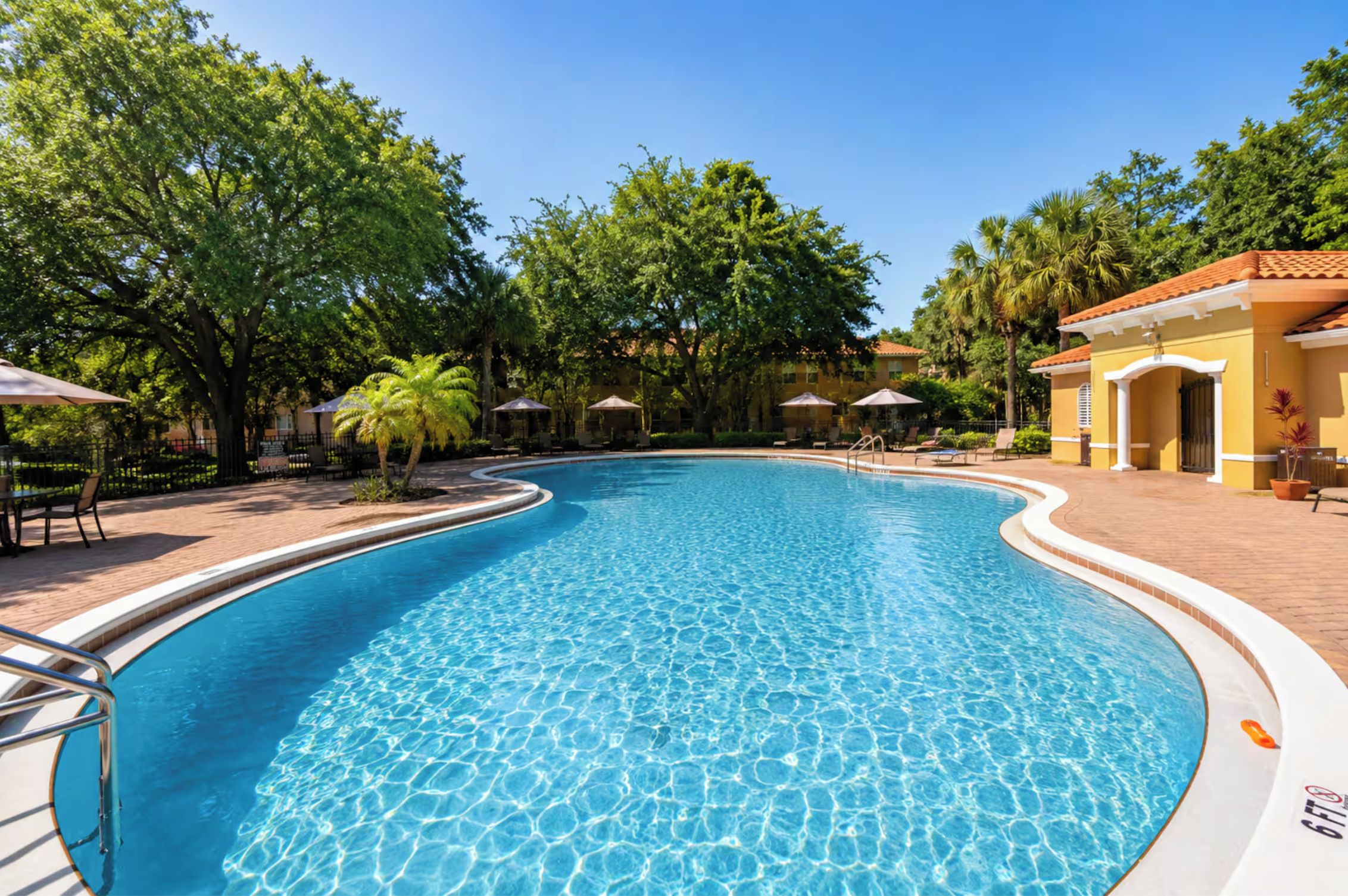 A clear blue swimming pool surrounded by trees and outdoor seating areas.