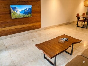 A modern dining area with a wooden table and chairs, a television mounted on a wooden wall, and a tiled floor. - Vimana Bali Seven Managed by AVM (Badung)