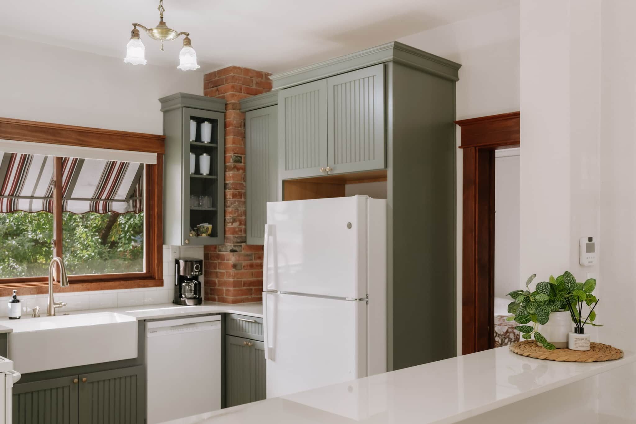 A kitchen with a refrigerator, a coffee maker, and a window with a view of trees.