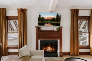 Una sala de estar con chimenea, un televisor montado sobre ella y vistas a un paisaje montañoso a través de las ventanas.