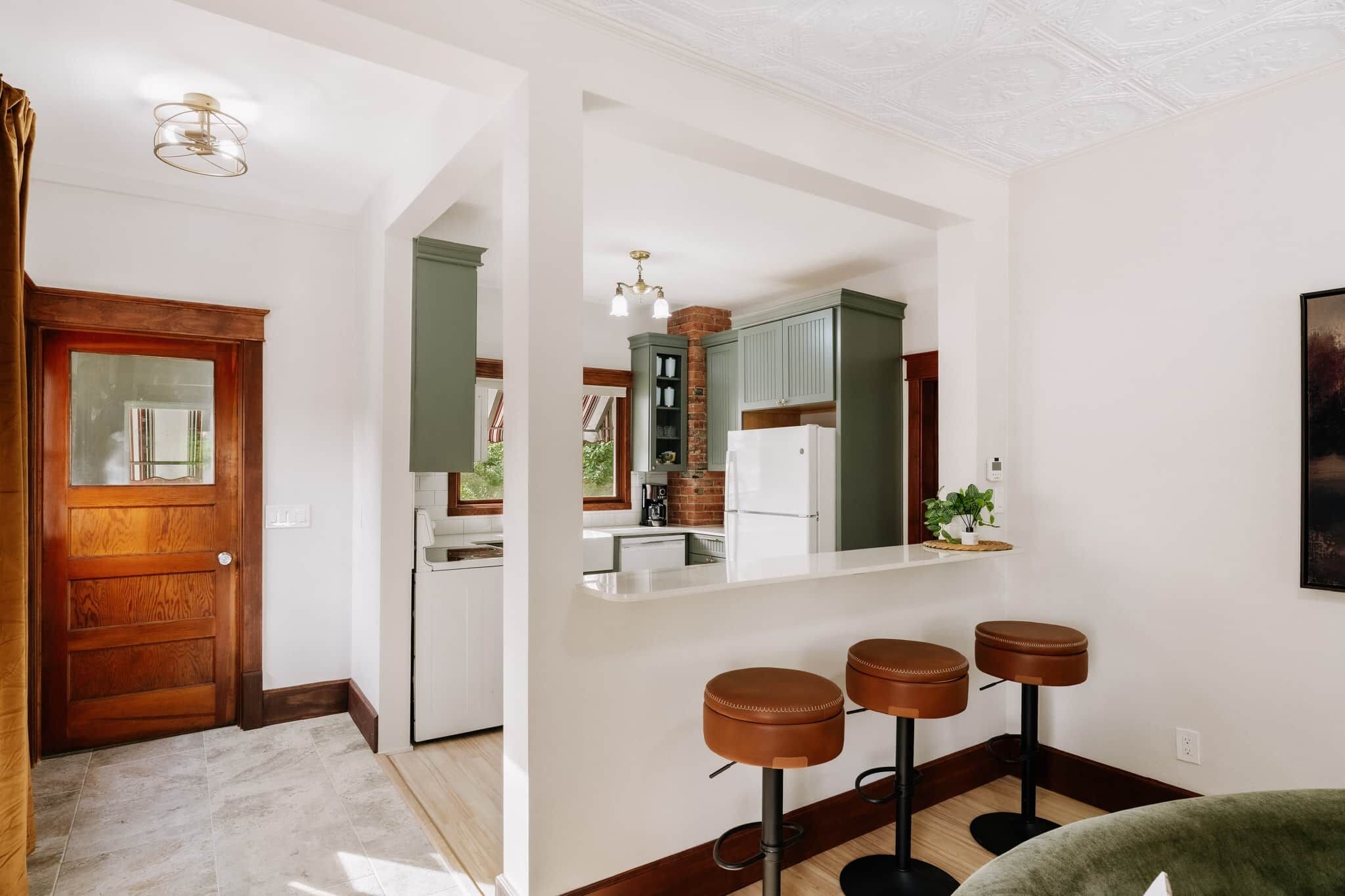A modern kitchen with a central island, bar stools, and a view into the dining area.