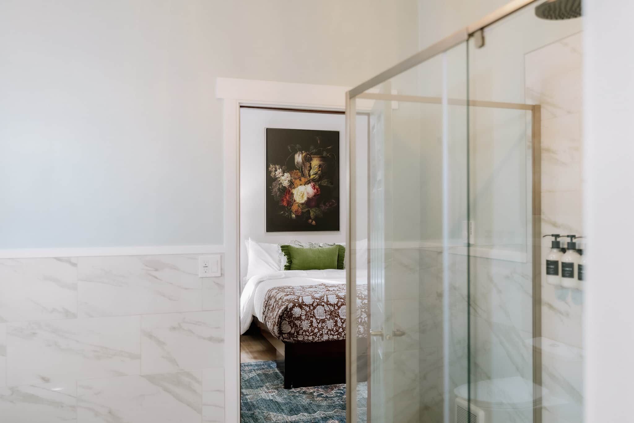 A hotel room with a bed, a glass shower enclosure, and a painting on the wall.