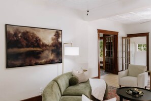 A living room with a large painting, a green sofa, a lamp, and a coffee table. - The Van Winkle House (Sheridan)