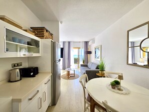 A modern kitchen with a built-in refrigerator, a dining area with a white table and chairs, and a living area with a sofa and a large window. - SR Romana Playa 811, directly on the beach (Marbella)