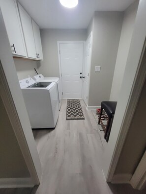 A laundry area with a washing machine and dryer, a door, and a small bench. - Charming 3-bedroom house in Southern Pines (Southern Pines)