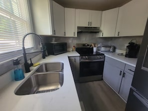A compact kitchen with a stainless steel sink, a microwave, a stove, and a toaster. - Charming 3-bedroom house in Southern Pines (Southern Pines)