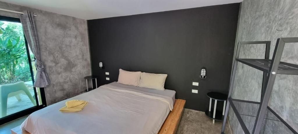 Een moderne slaapkamer met een groot bed, een klein nachtkastje, een wandplank en uitzicht op groen buiten.