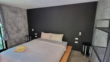 Een moderne slaapkamer met een groot bed, een klein nachtkastje, een wandplank en uitzicht op groen buiten.