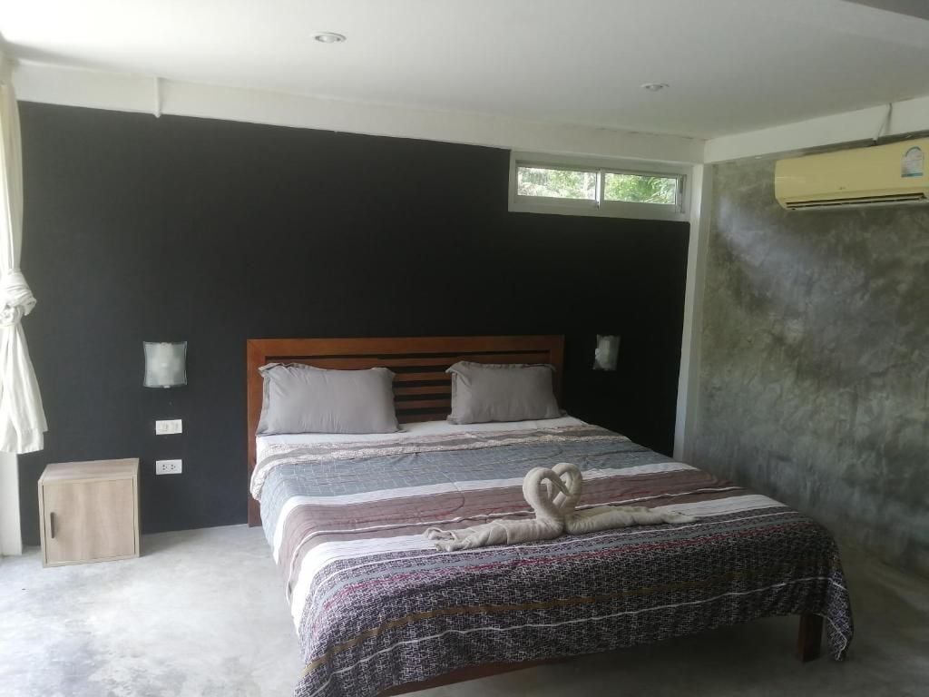 A bedroom with a bed, a window, a wall-mounted air conditioner, and a small cabinet.