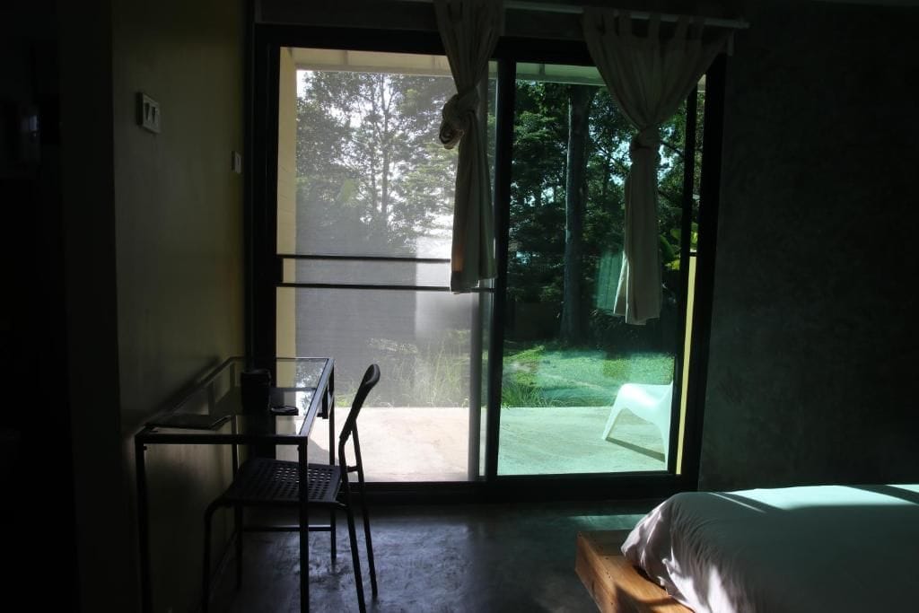 Ein Zimmer mit einem Bett, einem Schreibtisch und einem Stuhl. Eine Glastür führt zu einem Außenbereich.