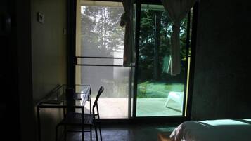 Ein Zimmer mit einem Bett, einem Schreibtisch und einem Stuhl. Eine Glastür führt zu einem Außenbereich.