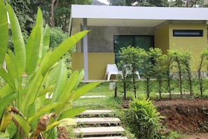 Edificio moderno con fachada amarilla, exterior blanco y un pequeño jardín con escalones que conducen a una silla blanca.