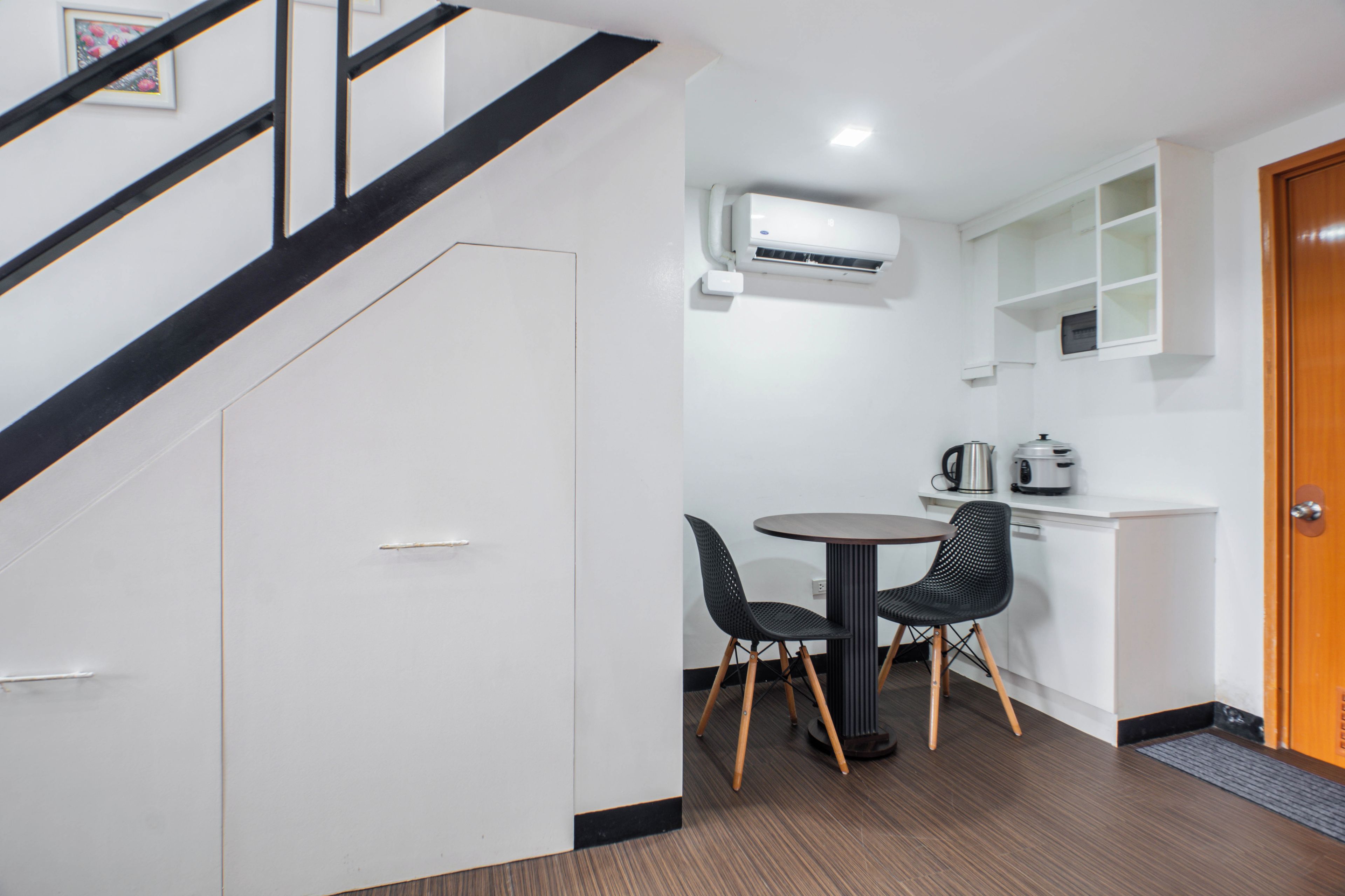 A modern kitchen with a dining table and chairs, a staircase, and a white wardrobe.