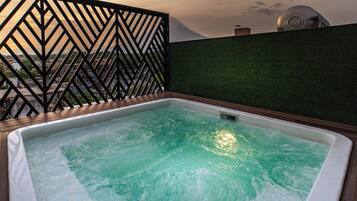 A hot tub with a view of a cityscape through a geometric metal fence.
