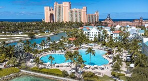 Een resort met een groot centraal zwembad, palmbomen en uitzicht op de oceaan.