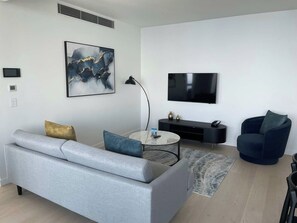 A modern living room with a grey sofa, a coffee table, a TV, and a black entertainment unit. - Panoramic Ocean Luxe Lv54  2Bed 2Bath Parking Inc (Broadbeach)