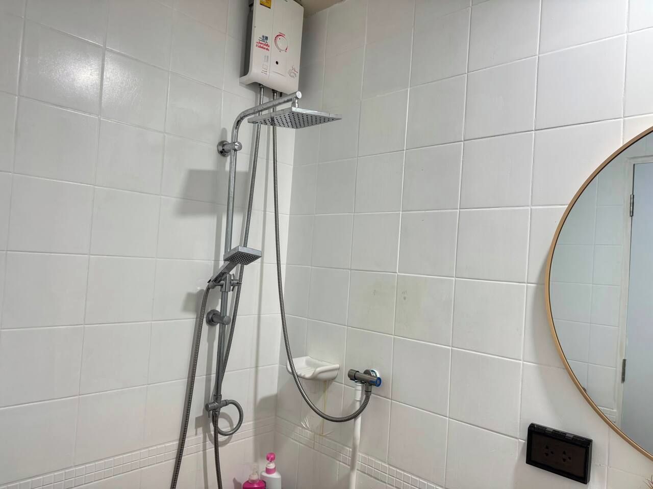 A bathroom with white tiled walls, a shower with a handheld showerhead, a handheld shower attachment, and a wall-mounted faucet.
