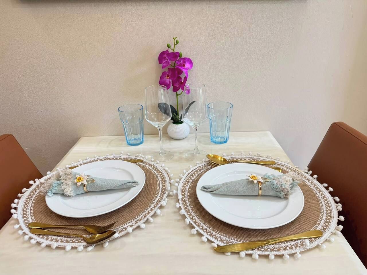 Une table dressée avec deux assiettes, des couverts et de la verrerie, et un vase de fleurs placé au centre.