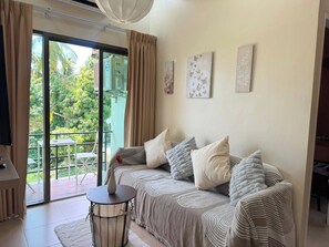 Een woonkamer met een bank, een klein rond tafeltje en uitzicht op een balkon met tuinmeubilair.