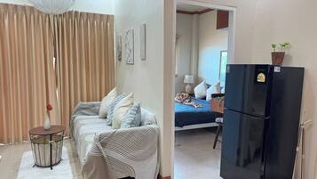 Een woonkamer met een bank, een ronde tafel, een zwarte koelkast en een bed op de achtergrond.