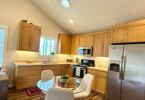 A modern kitchen with wooden cabinets, stainless steel appliances, and a glass dining table. - The Poulsbo Cottage - Walk to Historic Downtown (Poulsbo)