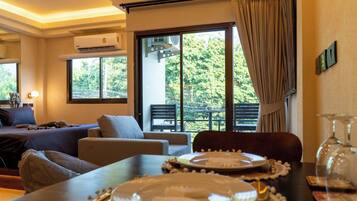 Hotelkamer met een bed, zithoek, eettafel gedekt voor twee personen en een balkon met uitzicht op groen.