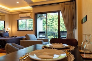 Une chambre d’hôtel comprenant un lit, un coin salon, une table à manger pour deux personnes et un balcon avec vue sur la verdure.