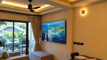 A hotel room with a large window, a ceiling fan, a flat-screen TV, a dining table with plates and glasses, and a cushioned seating area.