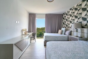Ein modernes Schlafzimmer mit zwei Betten, einem Schreibtisch und Blick auf Grünflächen.
