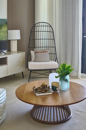 Ein modernes Wohnzimmer mit einem runden Holztisch, einem schwarzen Drahtstuhl mit Kissen, einem weißen Sofa, einer Lampe und einer Topfpflanze.