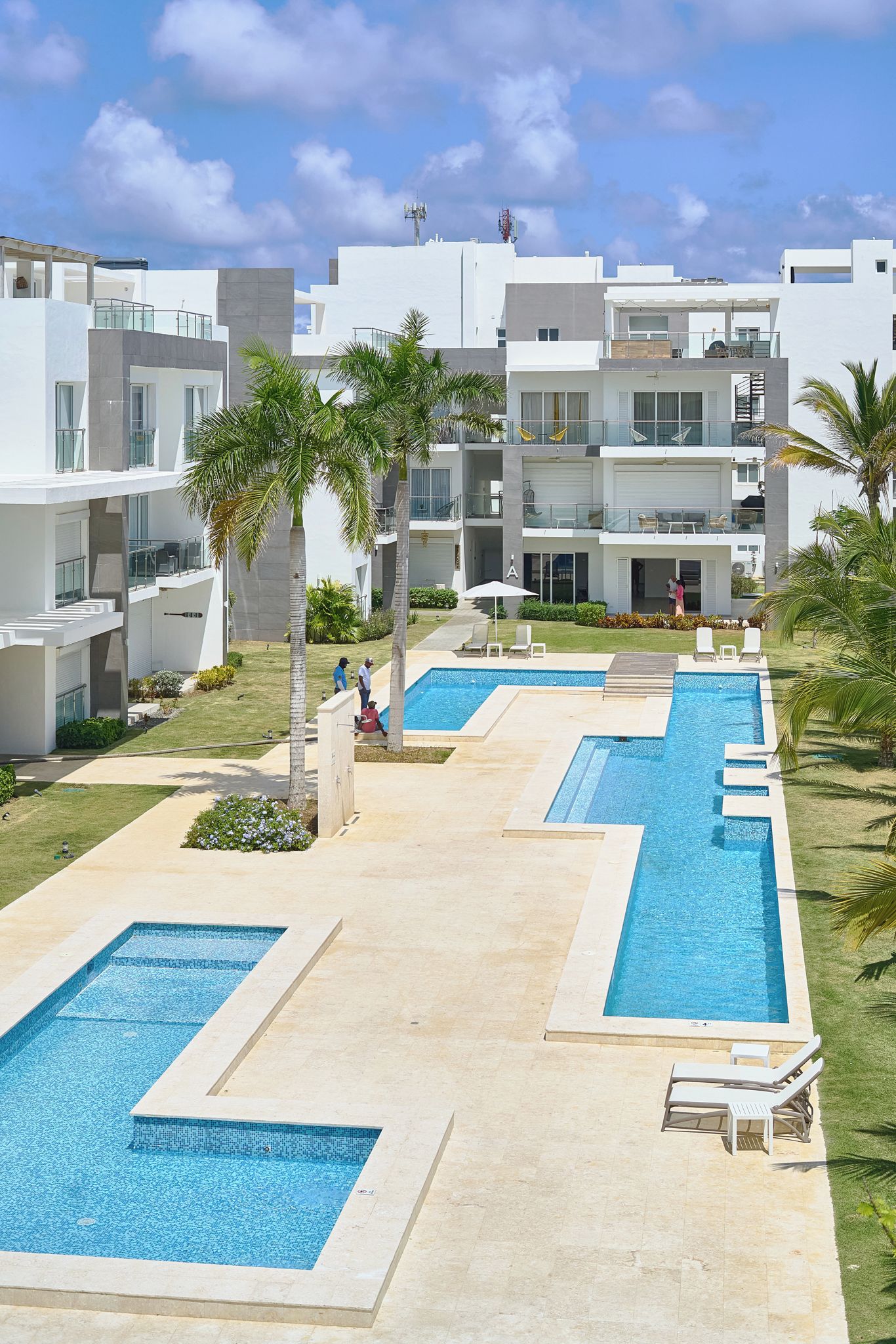 Ein modernes Resort mit mehreren Schwimmbecken, Palmen und blauem Himmel.