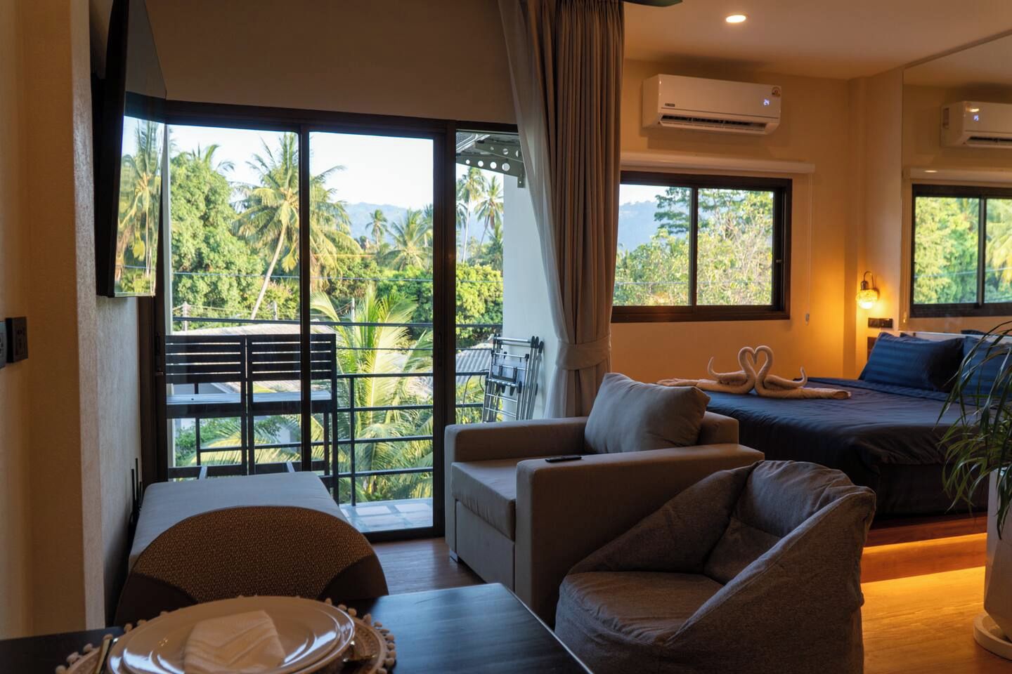 Une chambre d’hôtel avec un balcon, un lit agrémenté d’un oreiller en forme de cygne, un canapé, une table à manger et un appareil de climatisation.
