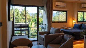 Een hotelkamer met balkon, een bed met een zwaan-vormig kussen, een sofa, een eettafel en een airconditioning.