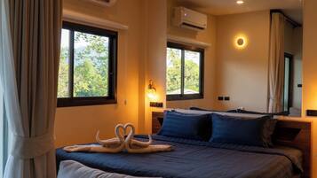 A hotel room with a bed, two windows, an air conditioning unit, and a wall-mounted lamp.