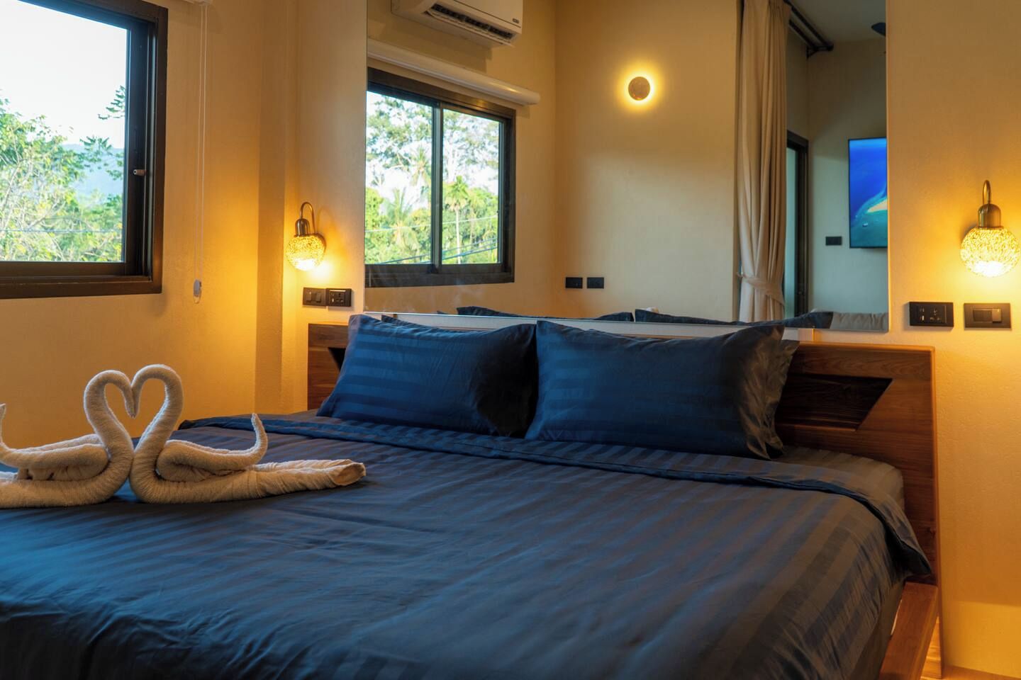Une chambre d’hôtel avec un lit, deux appliques murales, une fenêtre et une vue sur la verdure.