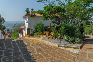 Una scala in pietra conduce a un edificio bianco con tetto in tegole, immerso nel verde e con vista su dolci colline.