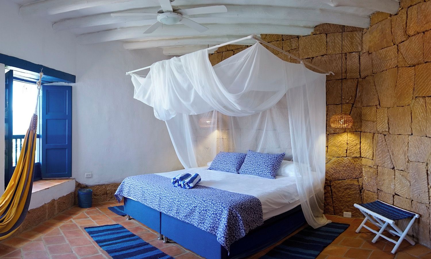 Een slaapkamer met een hemelbed, een stenen muur en een hangmat.