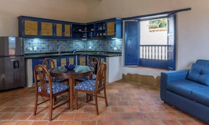 Una cucina compatta con mobili blu, un tavolo da pranzo con sedie, un frigorifero e un divano blu in un angolo.
