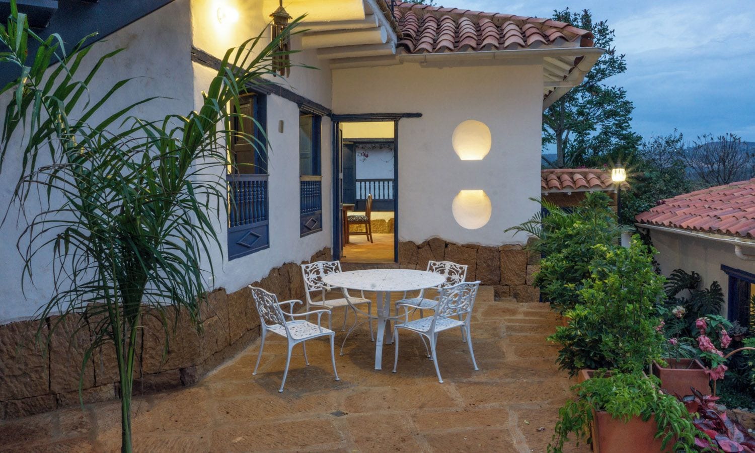 A patio with a round table and chairs, surrounded by potted plants and a stone wall.
