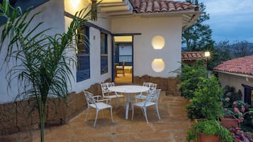 A patio with a round table and chairs, surrounded by potted plants and a stone wall.